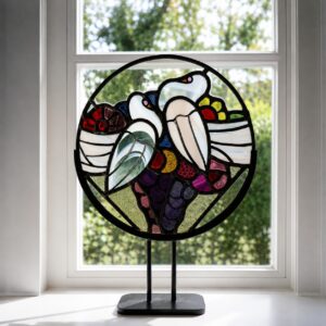 Handgemaakt glas in lood kunstwerk met twee duifjes op zwarte standaard voor het raam.