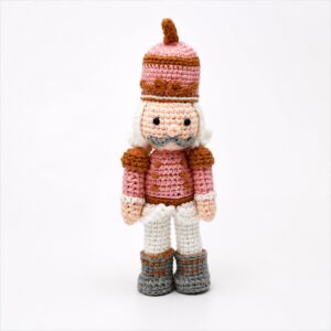 Gehaakte notenkraker in roze van 25 cm met hoge muts, witte broek en grijze laarsjes.