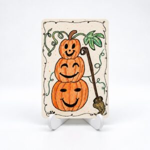 Handbeschilderde Halloweenkaart Drie keer pompoenpret van By Mieke met drie gestapelde oranje pompoenen en een bezem.