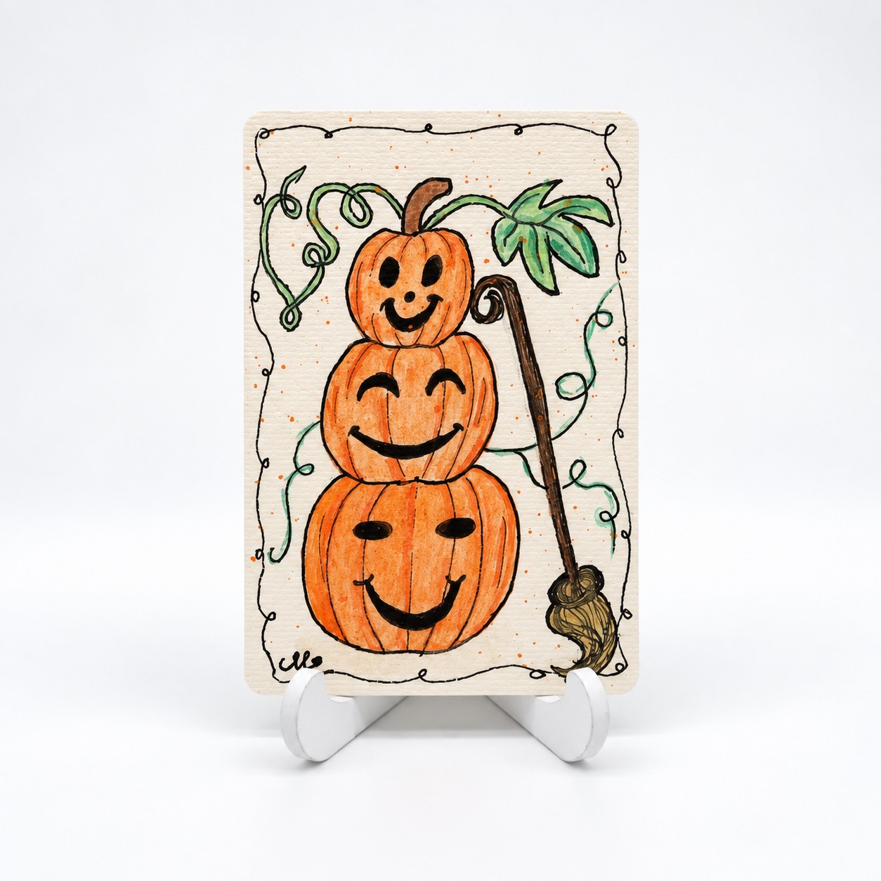 Handbeschilderde Halloweenkaart Drie keer pompoenpret van By Mieke met drie gestapelde oranje pompoenen en een bezem.